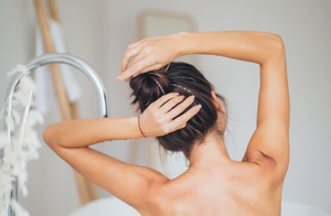 Close up image of a woman turned showing her shoulders as she relaxingly treats her brunette hair in the bathtub
